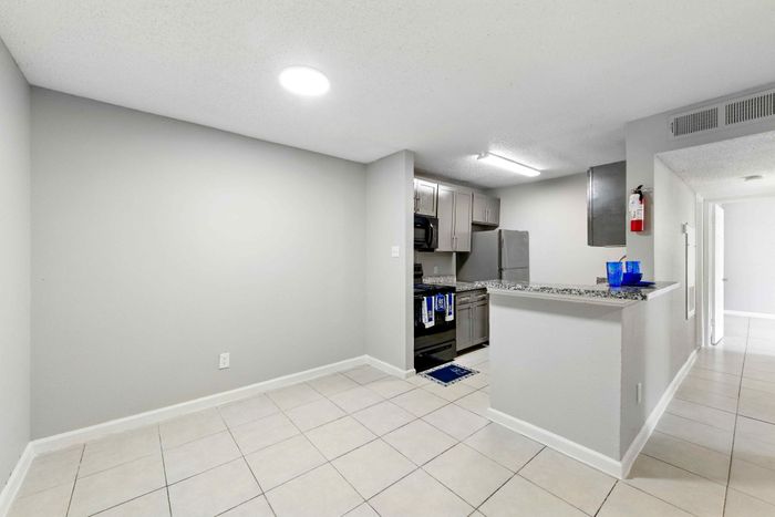 Chic apartment interior with a modern open kitchen, featuring sleek granite countertops and stainless steel appliances, adjacent to a spacious tiled area.