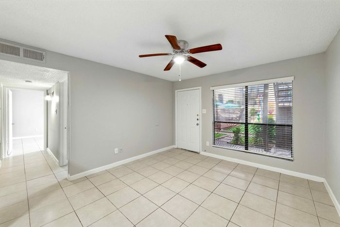 Bright and inviting living room with elegant tile flooring, large window with garden view, and ceiling fan for comfort.