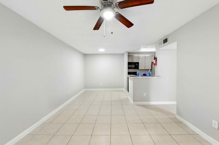 Modern, open-concept living and dining area featuring sleek tiled flooring, a ceiling fan, and a contemporary kitchen with granite countertops.