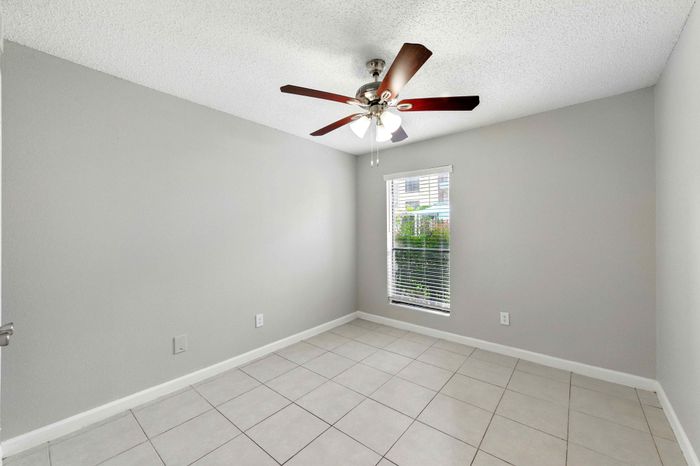 Bright, airy room with neutral tones and large window, featuring sleek tile flooring and modern ceiling fan, designed for comfort and style.