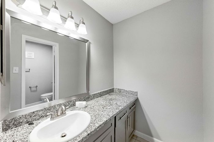 Elegant bathroom featuring a sleek granite countertop, modern fixtures, and a large mirror with contemporary lighting.