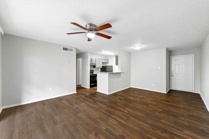 Bright and airy apartment living area with sleek hardwood floors, modern ceiling fan, and open-concept kitchen.