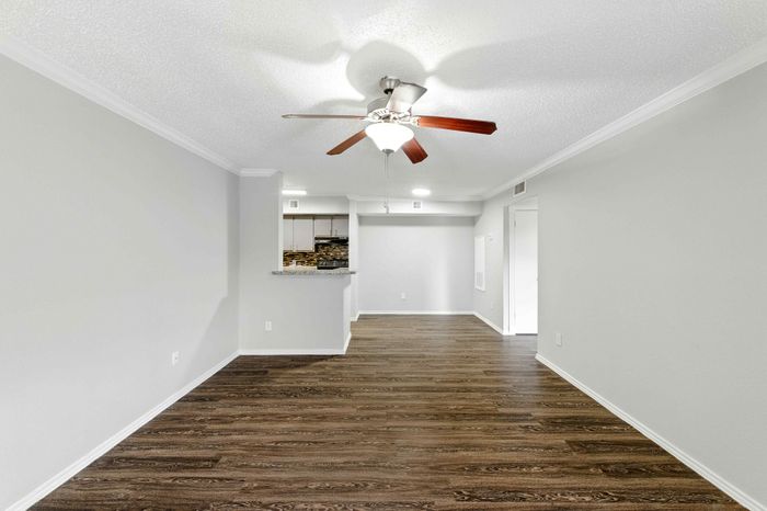 Bright open-concept living area with sleek hardwood floors, modern ceiling fan, and stylish kitchen passthrough.