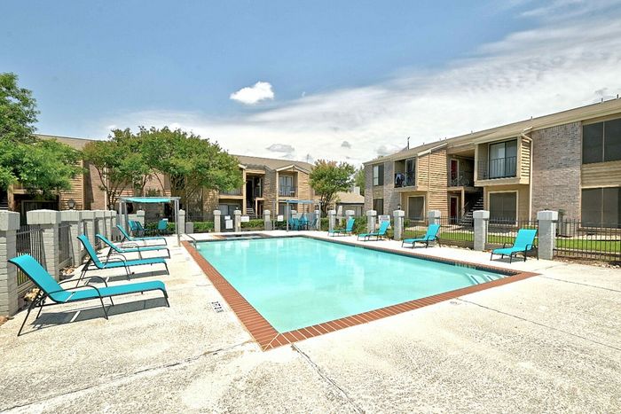 Inviting apartment complex with a sparkling pool, surrounded by comfortable lounge chairs and lush greenery, perfect for relaxation and leisure.