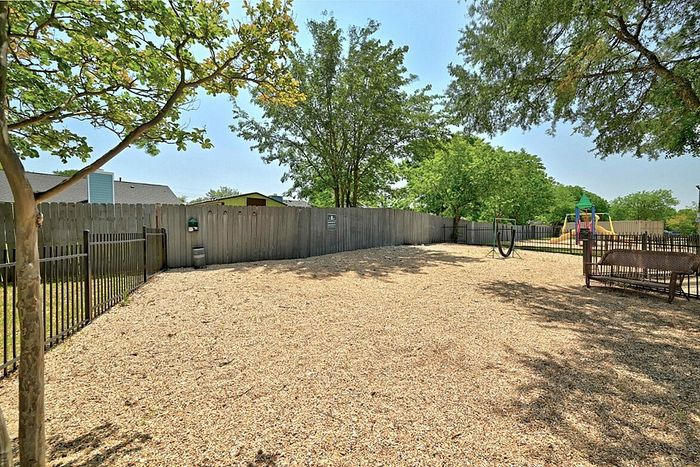 Inviting fenced outdoor area featuring mature trees, a cozy seating option, and a colorful children's playground, perfect for family enjoyment.