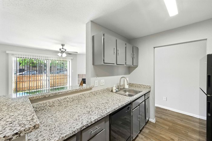 Contemporary kitchen with sleek granite countertops, modern fixtures, and open plan leading to a bright living area with sliding glass doors.