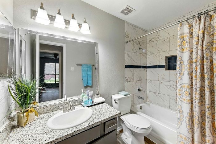 Modern bathroom featuring elegant granite countertops, stylish lighting, and a luxurious bathtub with patterned shower curtain.