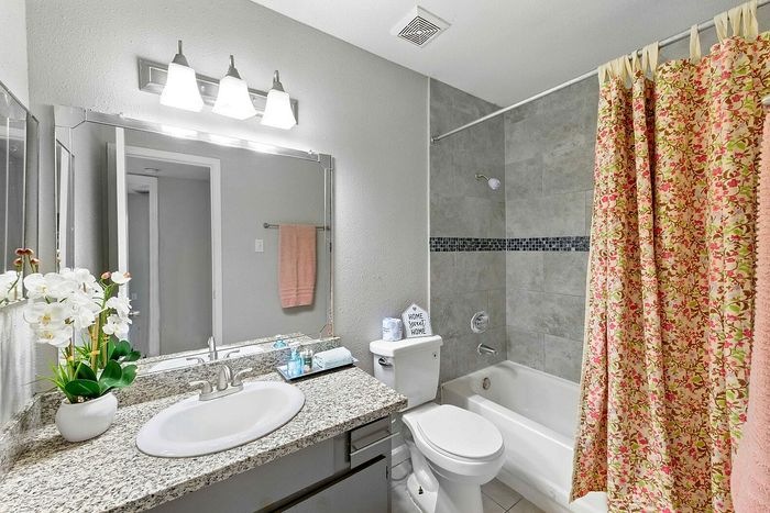 Bright and inviting bathroom with floral shower curtain, elegant granite countertop, and a chic vase of white orchids.