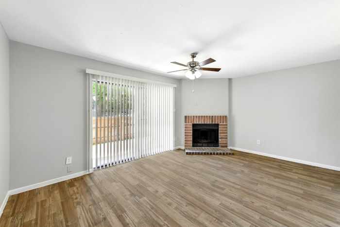 Bright, modern apartment living room with elegant hardwood floors, a cozy brick fireplace, and abundant natural light from large windows and sliding doors.