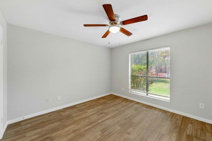 Bright and inviting room with elegant wood flooring, large window with garden view, and modern ceiling fan.