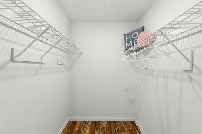 Spacious walk-in closet with elegant wooden flooring, pristine white shelving, and a welcoming 'Home' d&eacute;cor accent.