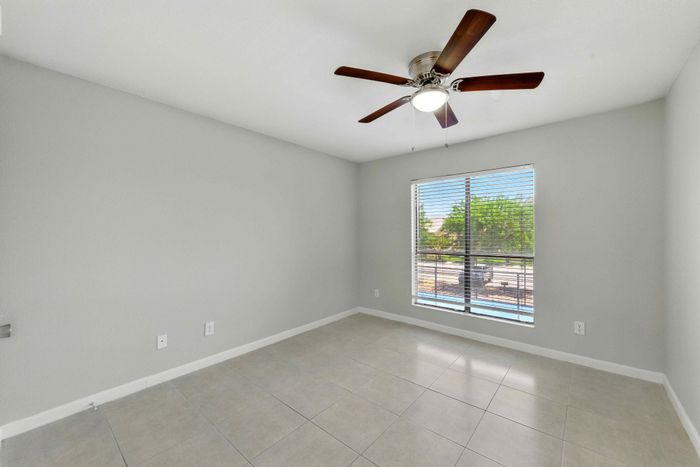 Bright and airy room with elegant ceiling fan, large window with view, and sleek tile flooring perfect for modern living.