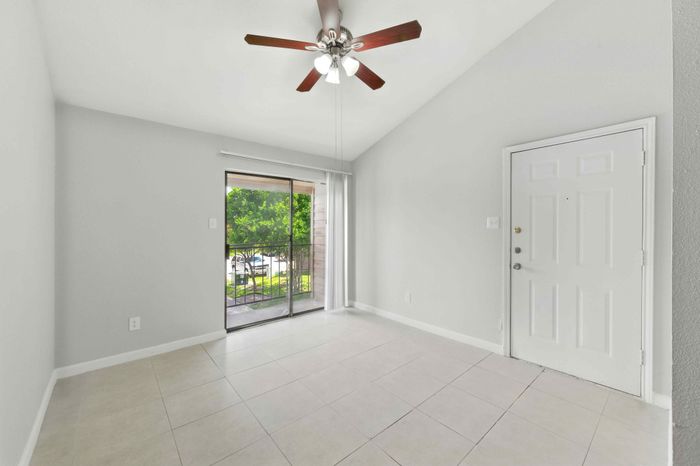 Bright, airy living space with elegant ceiling fan and large sliding glass door leading to a charming balcony with lush outdoor views.