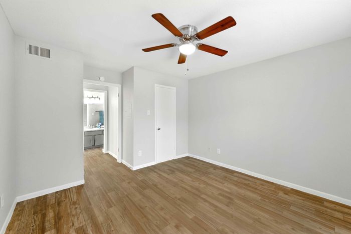Bright and spacious modern room with elegant wood flooring and a sleek ceiling fan, leading to a stylish bathroom.