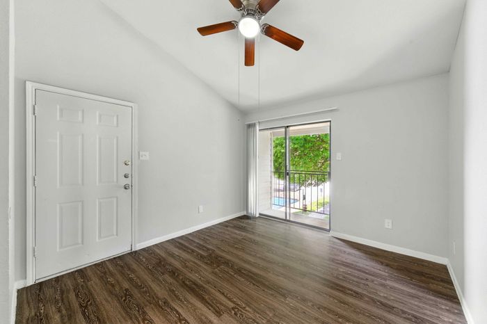 Bright and airy room with wood flooring and a ceiling fan, featuring a sliding glass door leading to a scenic balcony view.