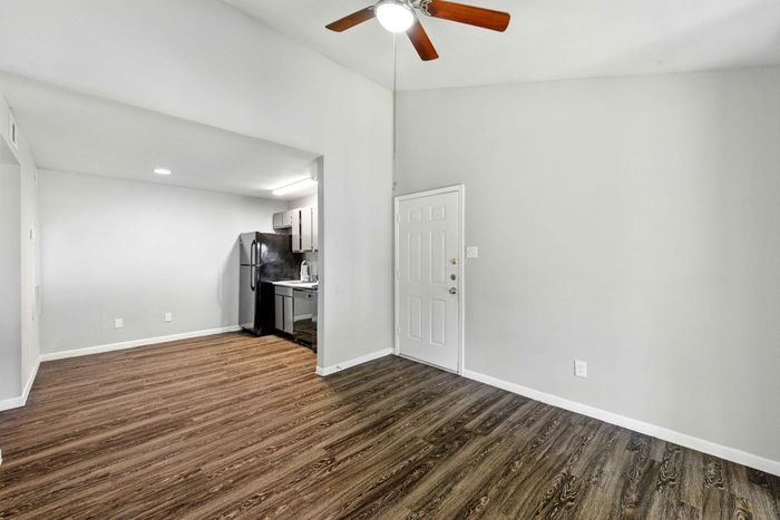 Charming open-plan apartment with sleek wood flooring, modern kitchen, and ceiling fan, perfect for a cozy living space.