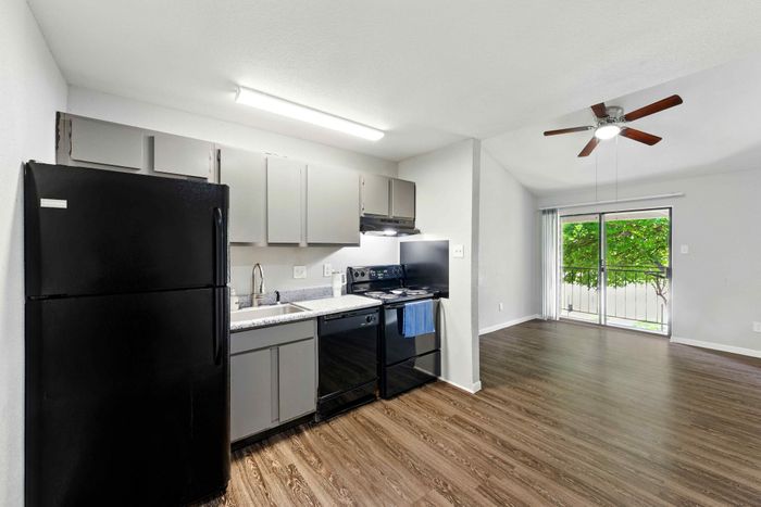 Modern kitchen with sleek black appliances and spacious open-plan living area featuring sliding glass doors and elegant wood flooring.
