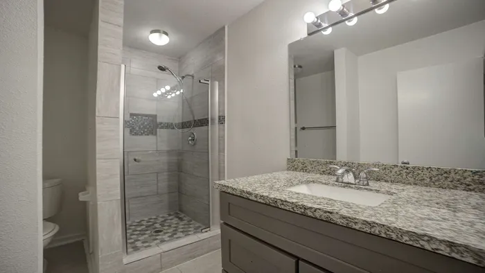 Modern bathroom featuring a sleek granite countertop, spacious glass-enclosed shower, and elegant lighting fixtures.
