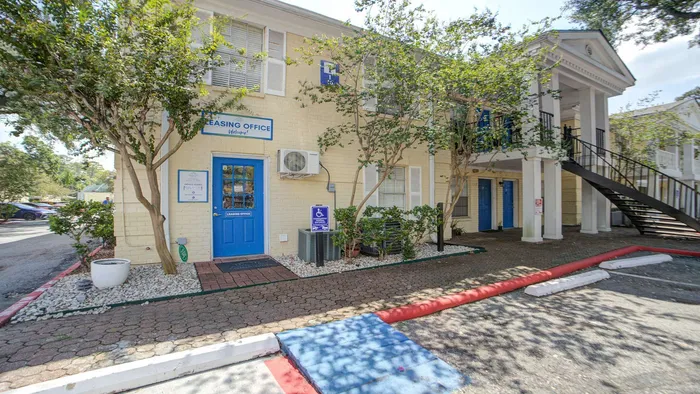 Charming two-story apartment exterior with elegant columns, blue entry doors, and lush green landscaping.