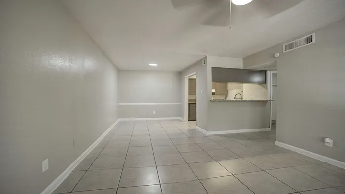 Spacious living area with sleek tile flooring, modern ceiling fan, and an open view into a stylish kitchen with granite countertops.