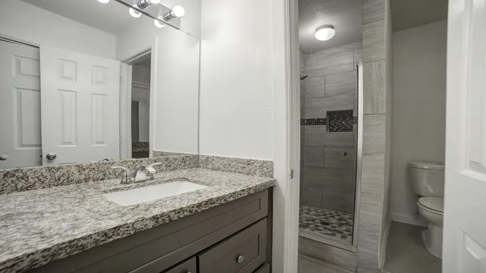 Elegant bathroom featuring a modern granite countertop, sleek vanity, and a stylish tiled shower for a luxurious touch.