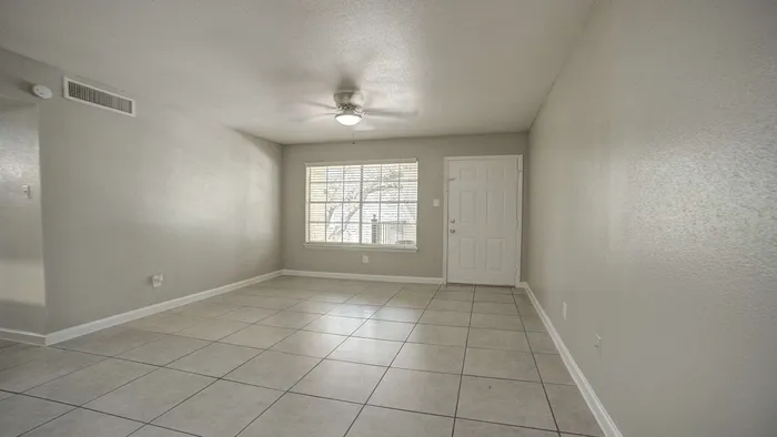 Bright and airy living room with modern tile flooring, neutral tones, and a large window inviting natural light.