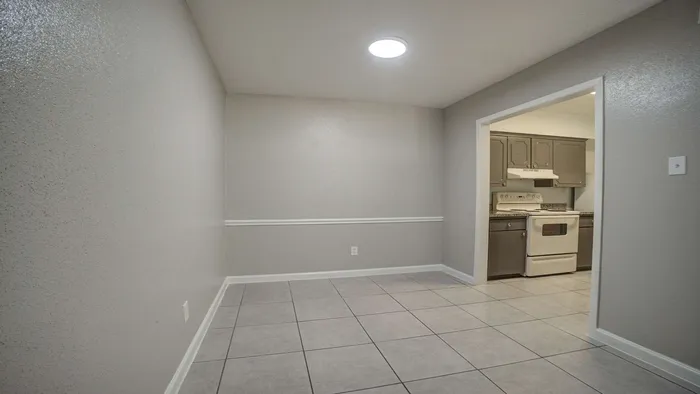 Modern dining area with sleek tiled flooring, adjacent to a cozy kitchen with classic cabinetry and a vintage-style stove.