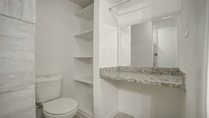 Modern bathroom with sleek granite countertop, spacious shelving, and pristine tile accents.