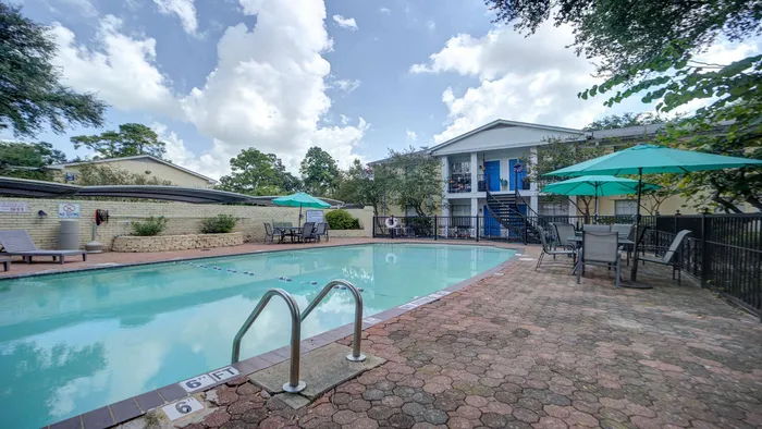 Inviting apartment complex with a refreshing swimming pool and stylish outdoor seating under vibrant umbrellas.