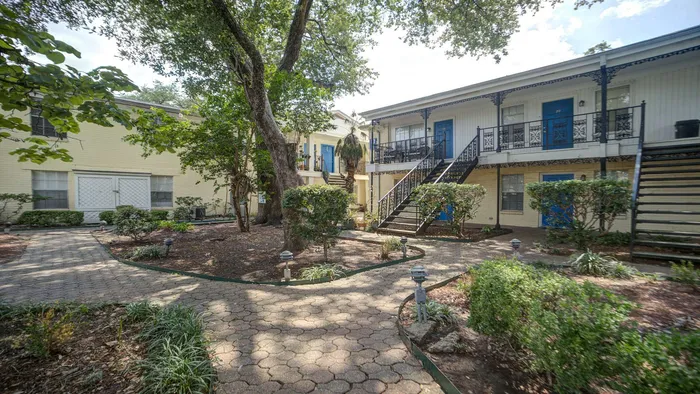 Charming apartment complex with lush garden paths, mature trees, and stylish wrought iron balconies.