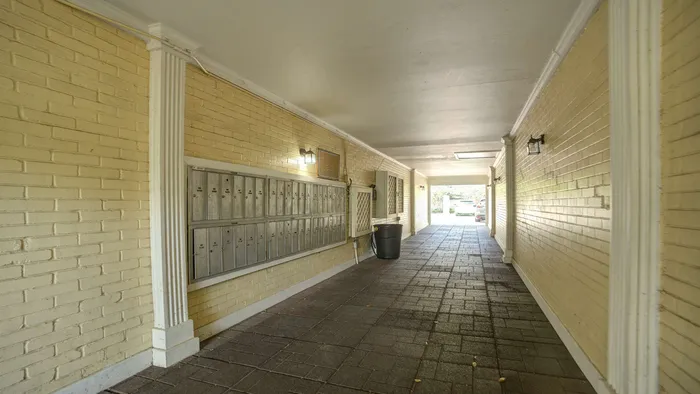 Inviting apartment corridor with stylish yellow brick walls, well-organized mailboxes, and elegant lighting, leading to a tranquil outdoor view.