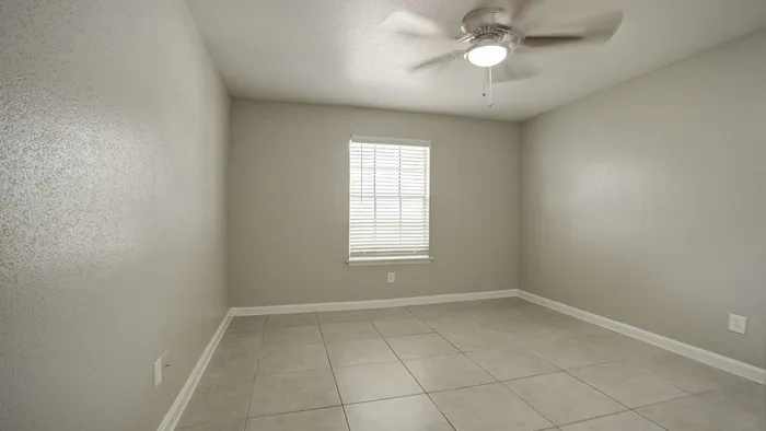 Bright and airy room with modern tiled flooring, soft gray walls, and elegant ceiling fan, ideal for cozy living.