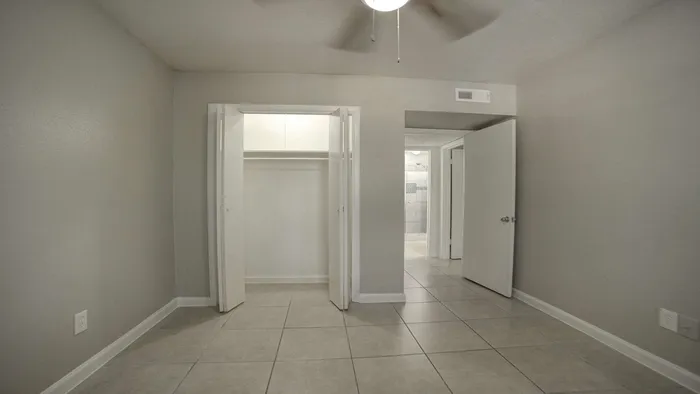 Contemporary room with neutral tones, featuring a spacious closet and elegant tiled flooring, leading to a modern bathroom.