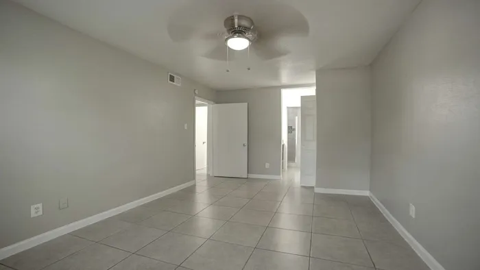 Contemporary empty room with sleek gray tile flooring, neutral walls, and a modern ceiling fan, perfect for customization.