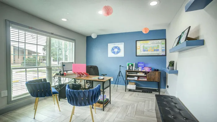 Bright modern office space with elegant blue chairs, wooden desk, and large window offering natural light.