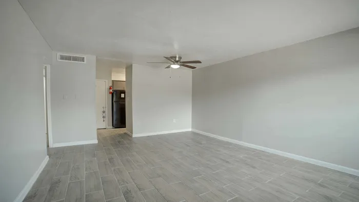 Charming living room with elegant wood-style flooring, modern ceiling fan, and seamless transition to a sleek kitchen with contemporary appliances.