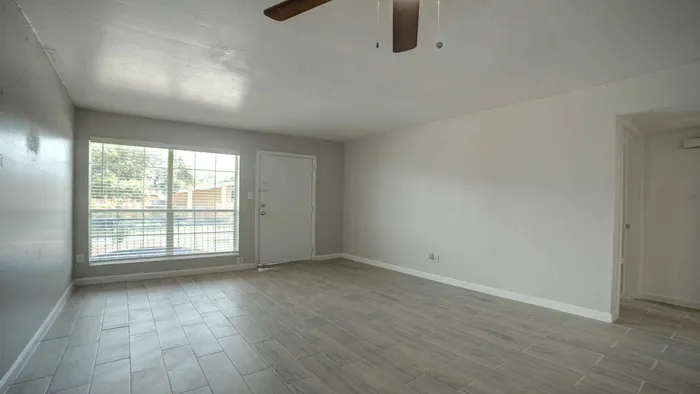 Bright and spacious living room with modern tile flooring and large window, offering natural light and outdoor views.