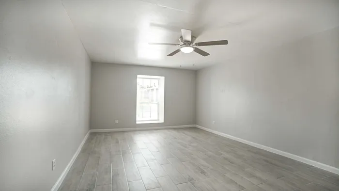 Bright, spacious room with sleek wood flooring, a modern ceiling fan, and a large window inviting natural light.