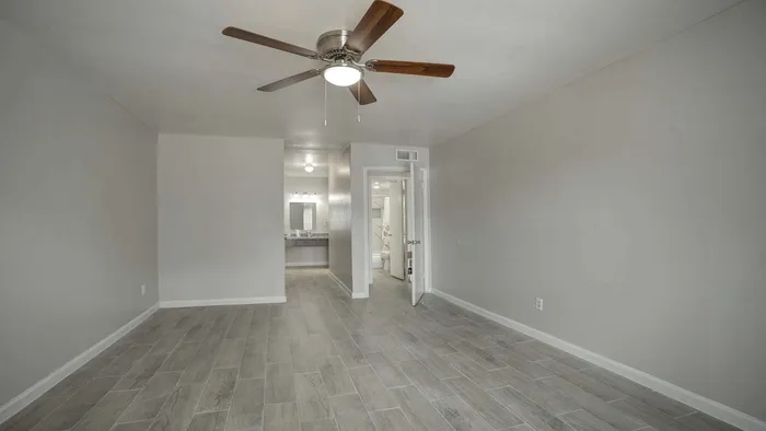 Bright and spacious room with modern ceiling fan, elegant gray tiled flooring, and view into a sleek bathroom area.