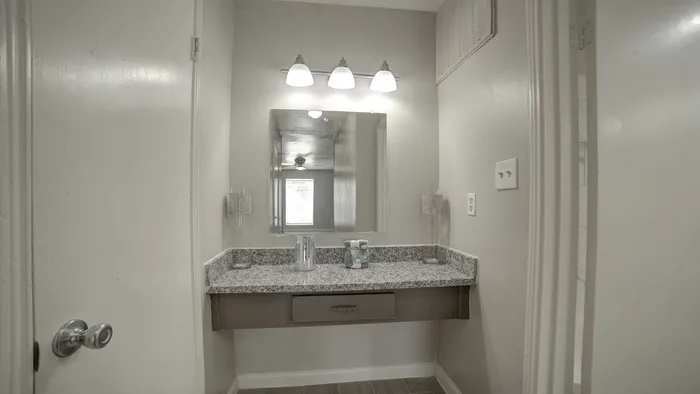 Elegant bathroom vanity with granite countertop, large mirror, and contemporary lighting, enhancing the apartment's modern feel.