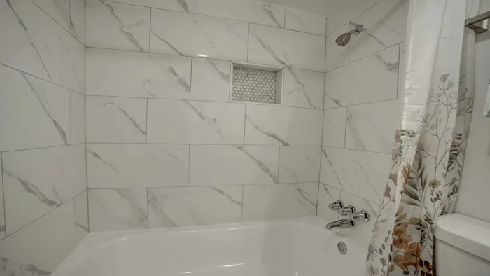 Elegant bathroom with modern white marble tiles and a sleek bathtub, accented by a floral shower curtain.