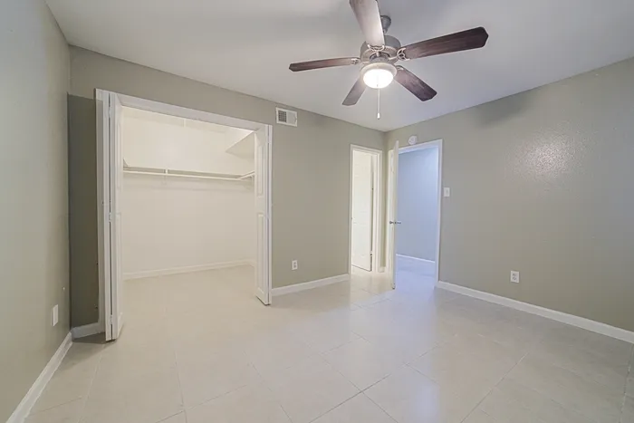 Bright, spacious bedroom with elegant tile flooring and a ceiling fan, featuring a large walk-in closet for ample storage.