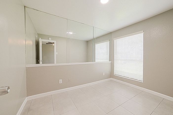 Bright, open room with large mirror, modern tile flooring, and natural light from a big window, ideal for versatile living or office space.