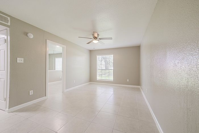 Bright and airy living room with modern ceiling fan and large window offering garden views, featuring sleek tile flooring and neutral-colored walls.