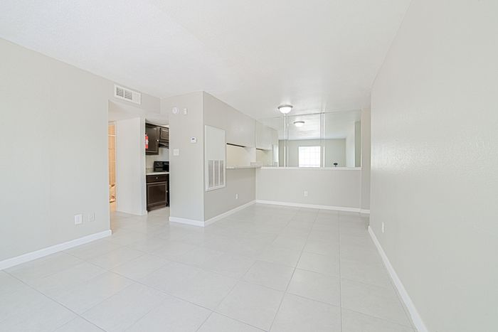 Bright apartment interior featuring a spacious open-plan layout with sleek white tiles and modern kitchen cabinetry.