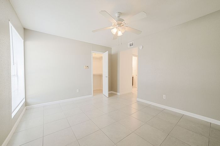 Bright, airy room with a ceiling fan, tiled floors, and open closet space, perfect for customizing your ideal living area.