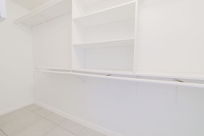 Spacious walk-in closet with ample shelving and hanging space, featuring sleek white finishes and modern tile flooring.