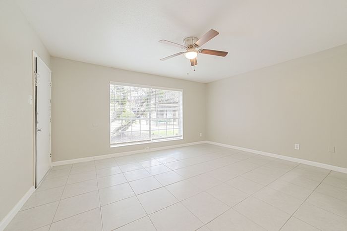 Bright and spacious living room with elegant tile flooring, large window, and modern ceiling fan, ideal for cozy gatherings.