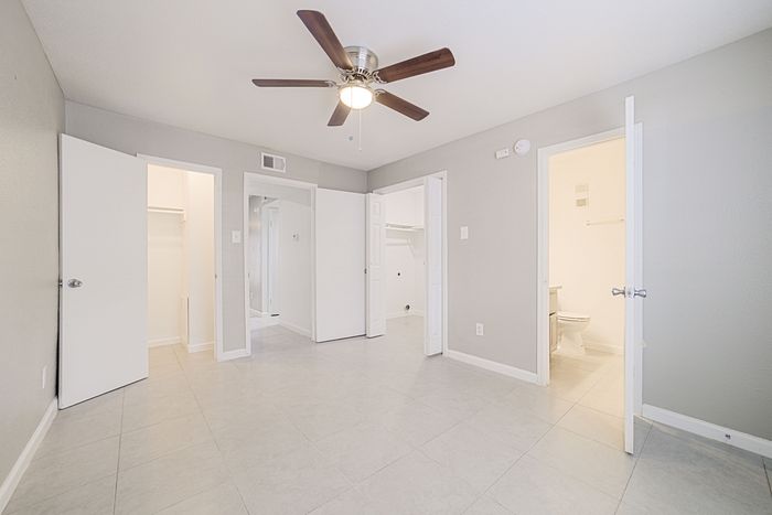 Bright and spacious room with modern tile flooring, ceiling fan, and multiple entryways leading to closets and bathroom; perfect for comfortable living.