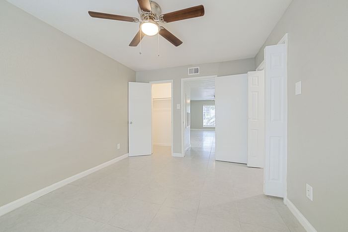 Bright, spacious bedroom with a modern ceiling fan, tiled floors, and ample closet space, leading to an inviting living area.